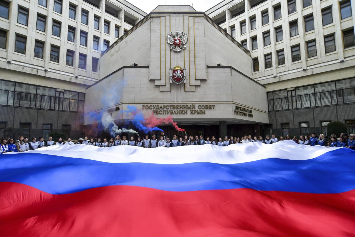 People hold a Russian national flag in front of the Crimean parliament while filming a youth action as a part of preparation to mark the ninth the anniversary of Crimea annexation from Ukraine in Simferopol, Crimea, Saturday, March 11, 2023. (AP Photo)