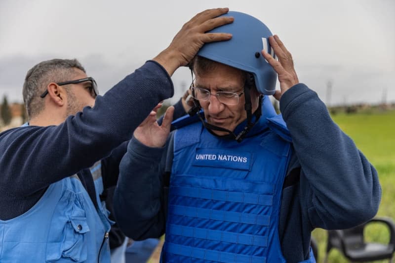 A member of the United Nations humanitarian delegation helps the United Nations Deputy Humanitarian Coordinator David Carden (R) putting a helmet during their visit to oversee the advancement of unexploded ordnance removal in Idlib. Anas Alkharboutli/dpa