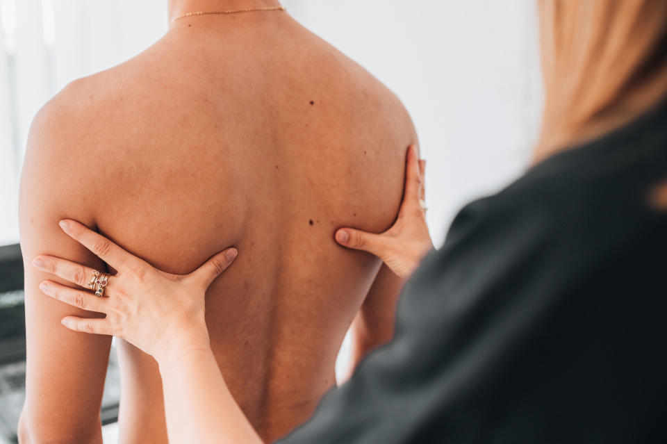 A person is being examined by a chiropractor, who is pressing their hands on the person's back to assess alignment