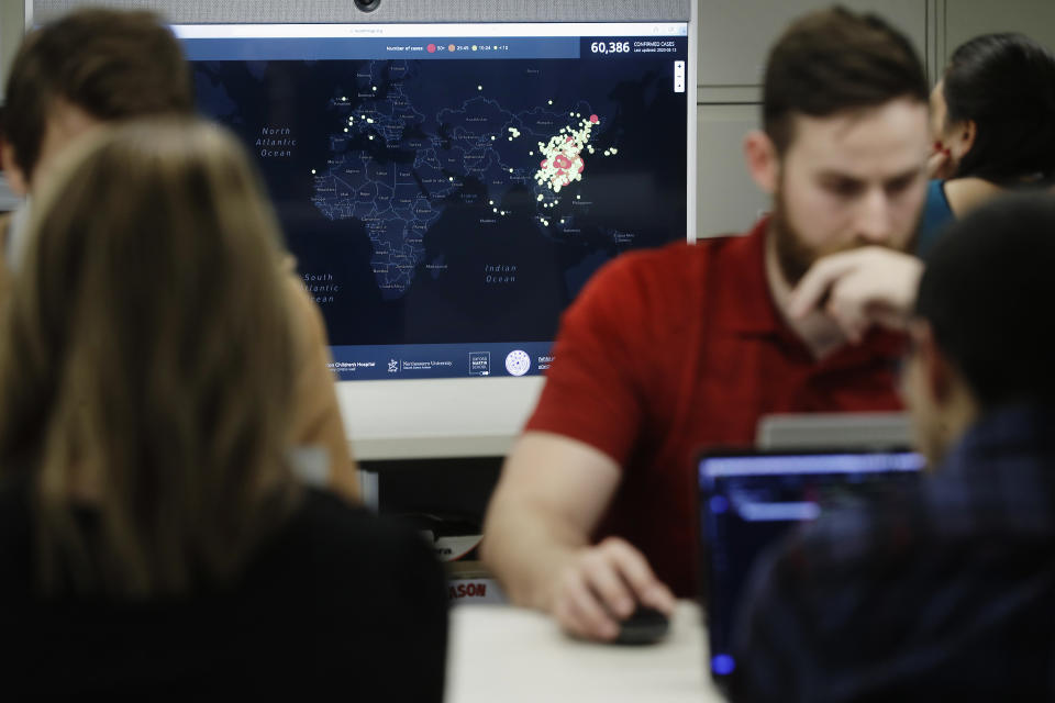 In this Thursday, Feb. 13, 2020 photo, Kyle Martin, a worker at HealthMap, a system using artificial intelligence to monitor global disease outbreaks, mines health data to keep the system up to date in a work area at Boston Children's Hospital in Boston. Early warnings of an emerging epidemic, some of them collected by HealthMap, showed AI's potential for giving global health experts a head start when bureaucratic hurdles and language barriers might get in the way. A screen behind displays a world map with colored dots marking cases of the disease known as COVID-19. (AP Photo/Steven Senne)