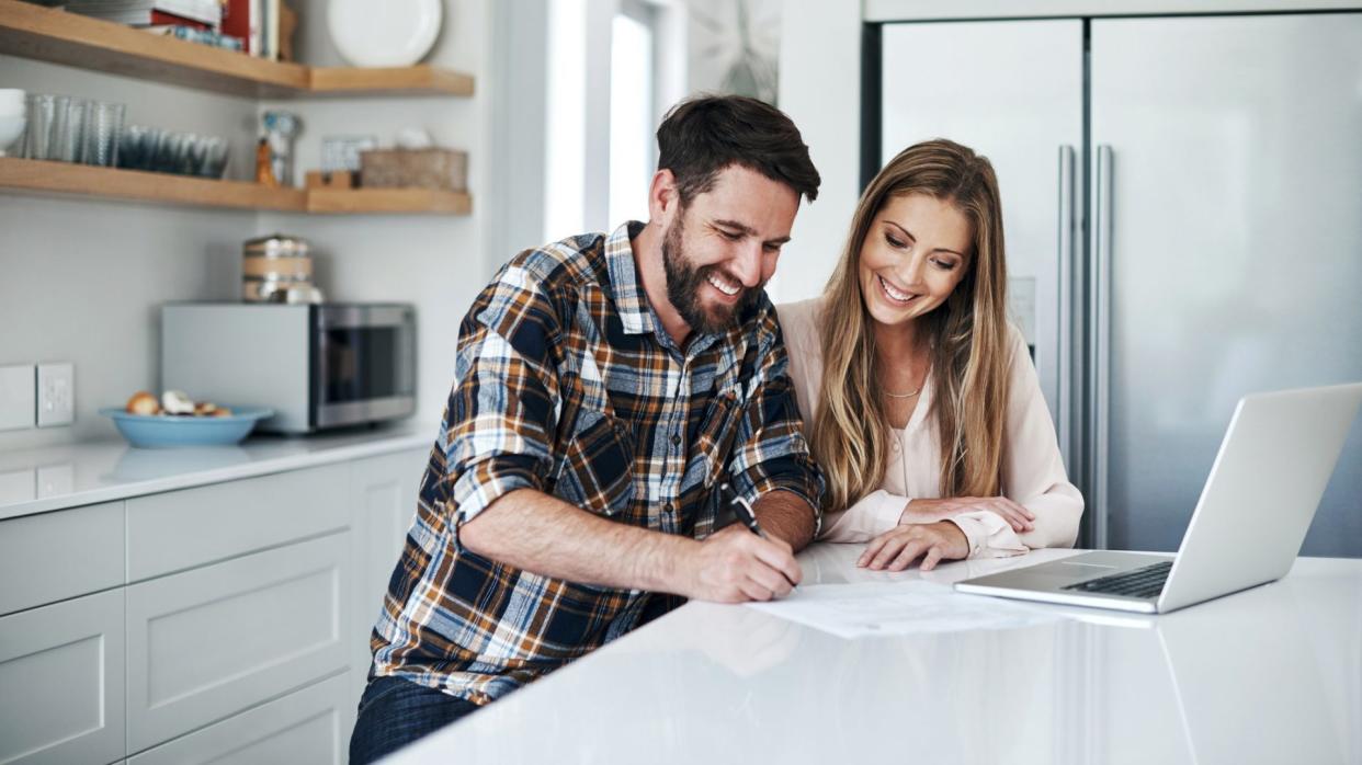 Shot of a young couple using a laptop and going through paperwork at home.