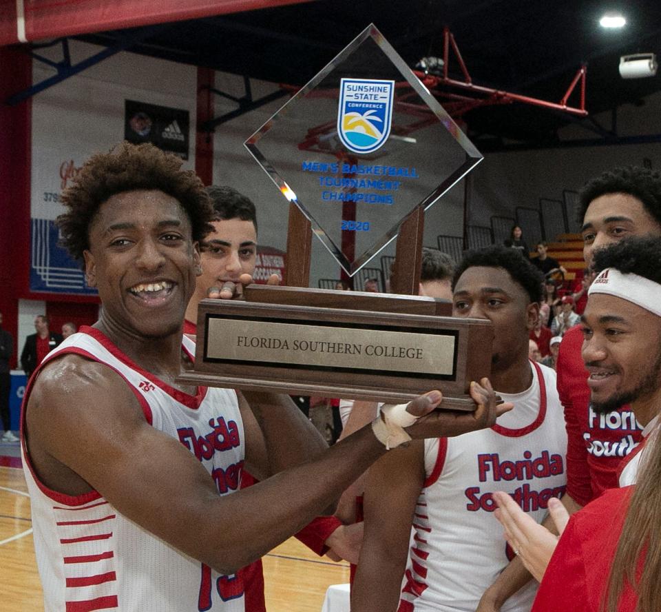 Florida Southern College's E.J. Dambreville (13) and fellow players smile as they hoist the SSC Tournament Championship trophy after their win over Nova Southeastern at Streamline Sale Arena at Jenkins Field House Sunday. March 8, 2020.