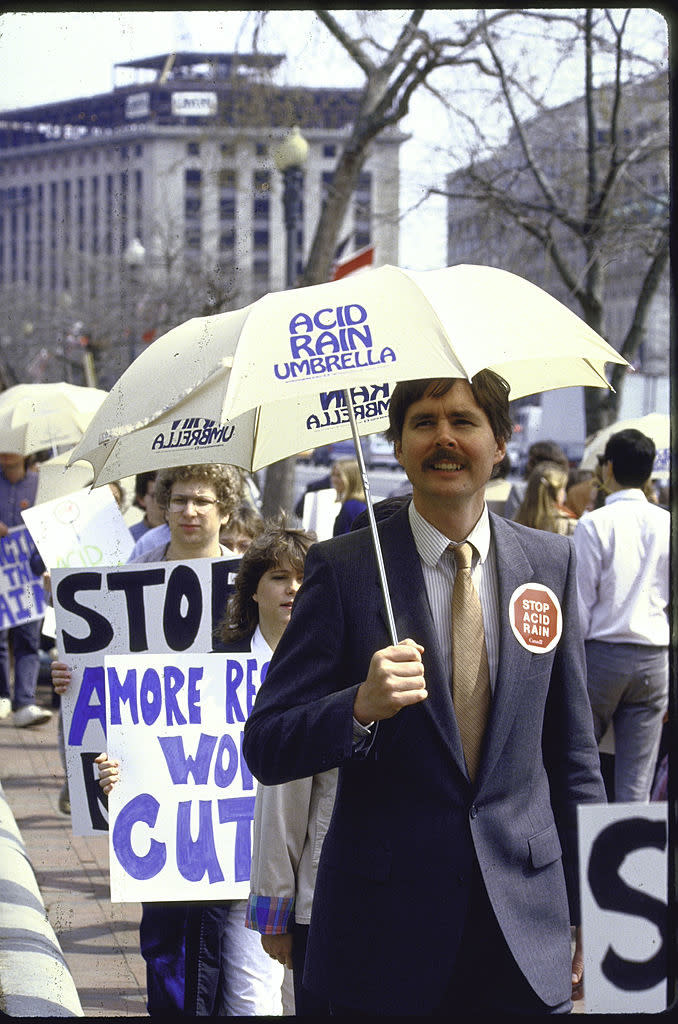 A man holding an "acid rain umbrella" and wearing a "stop acid rain" sticker in a crowd of protesters