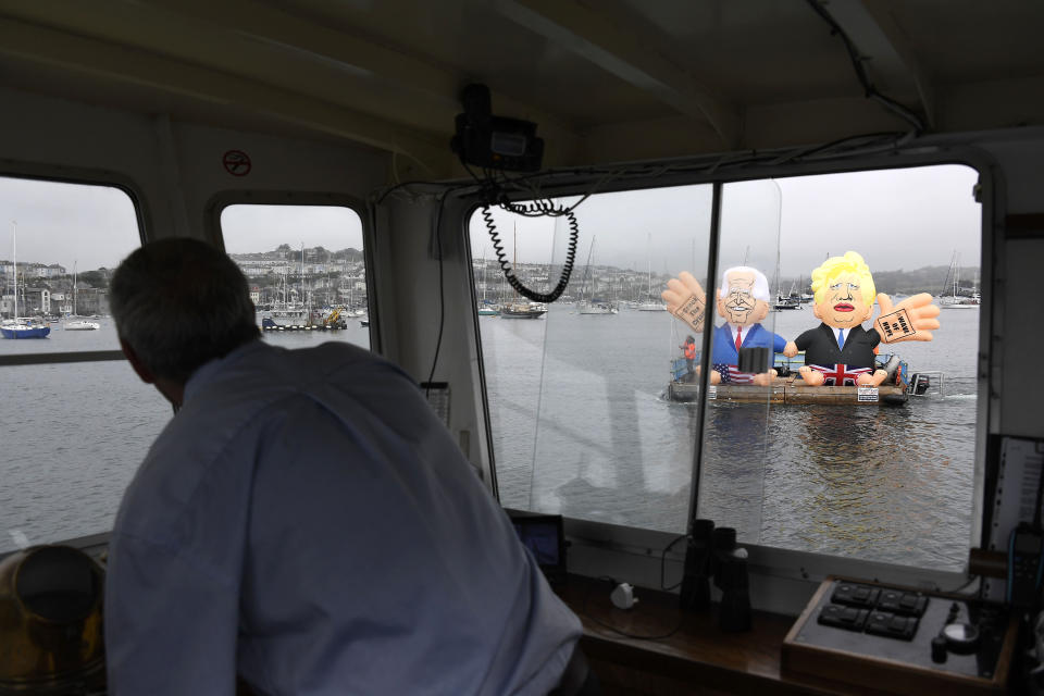 A captain steers his boat around giant balloons depicting U.S. President Joe Biden, left, and British Prime Minister Boris Johnson during a 'crack the crisis' action by NGO's in the harbour of Falmouth, Cornwall, England, during an action by NGO's on Friday, June 11, 2021. (AP Photo/Alberto Pezzali)