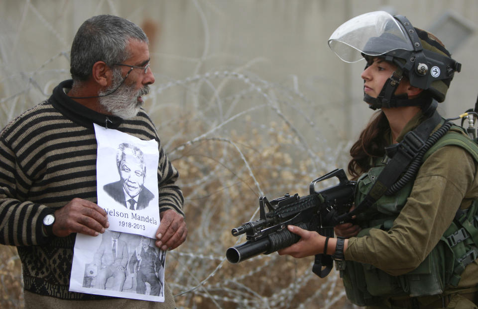 FILE - A Palestinian demonstrator holds portraits of late South African Leader Nelson Mandela and late Palestinian leader Yasser Arafat as he stands in front of Israeli soldier during a weekly demonstration against Israel's separation barrier, in the West Bank village of Bilin, near Ramallah, Dec. 6, 2013. Israel on Monday, Jan. 31, 2022, called on Amnesty International not to publish an upcoming report accusing it of apartheid, saying the conclusions of the London-based international human rights group are “false, biased and antisemitic.” (AP Photo/Majdi Mohammed, File)