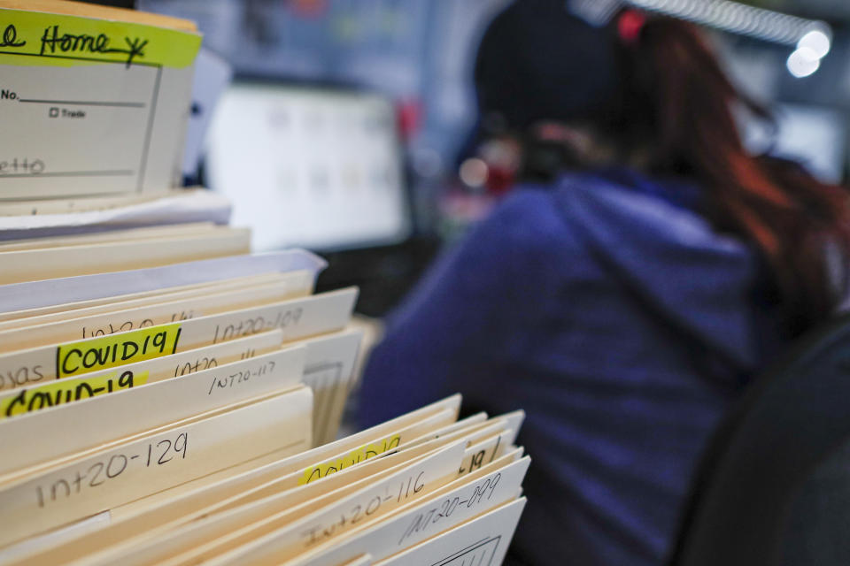 Folders containing information on those who died from COVID-19 are stacked amongst other clients while employee Gina Hansen works at Daniel J. Schaefer Funeral Home, Thursday, April 2, 2020, in the Brooklyn borough of New York. (AP Photo/John Minchillo)