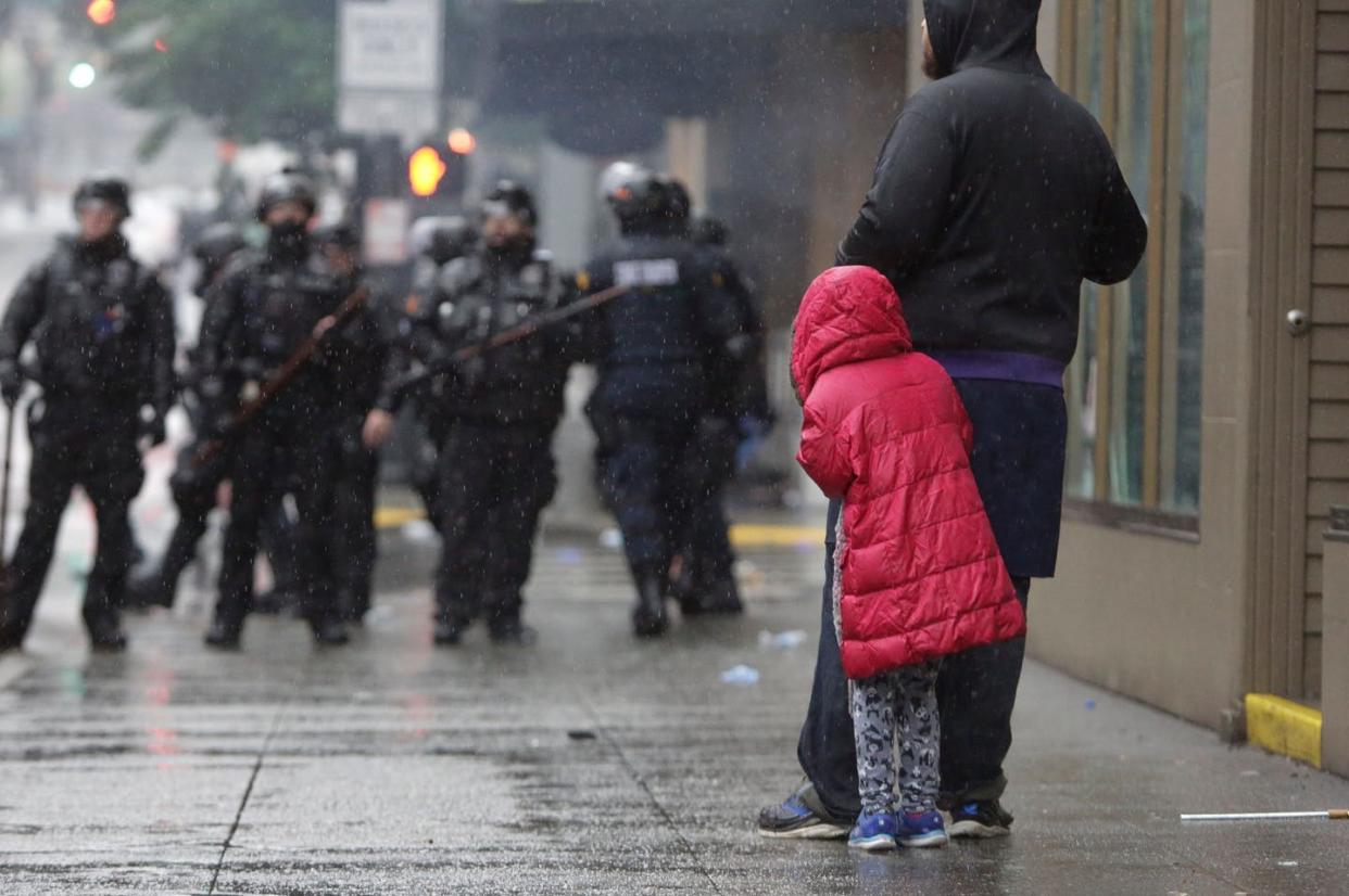 <span class="caption">Taking a peek, but probably not seeing a future career.</span> <span class="attribution"><a class="link " href="https://www.gettyimages.com/detail/news-photo/girl-holds-on-to-an-adult-as-police-in-riot-gear-stand-news-photo/1216441511?adppopup=true" rel="nofollow noopener" target="_blank" data-ylk="slk:Jason Redmond/AFP via Getty Images;elm:context_link;itc:0;sec:content-canvas"> Jason Redmond/AFP via Getty Images</a></span>