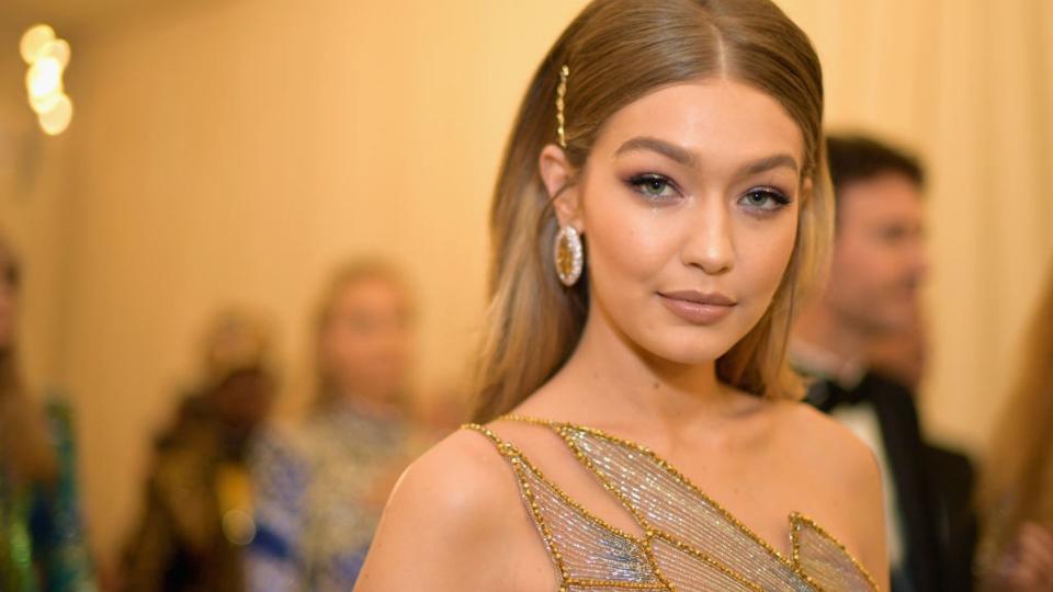 Gigi Hadid smiles at camera while wearing big earrings and sparkling gown. 