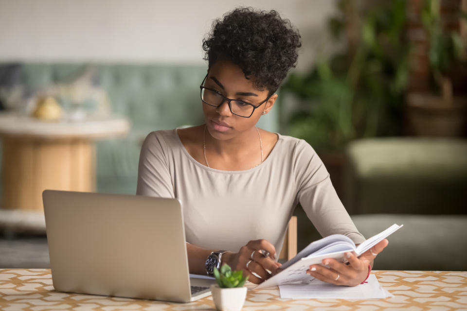 Woman reading a book with a laptop on the table, possibly researching relationship advice