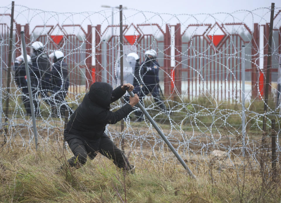 A man pulls down the fence during clashes with Polish border guards at the Belarus-Poland border near Grodno, Belarus, on Tuesday, Nov. 16, 2021. Polish border forces say they were attacked with stones by migrants at the border with Belarus and responded with a water cannon. The Border Guard agency posted video on Twitter showing the water cannon being directed across the border at a group of migrants in a makeshift camp. (Leonid Shcheglov/BelTA via AP)