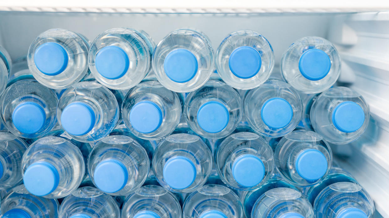 Rows of many transparent plastic bottles with drinking water supply in white refrigerator.