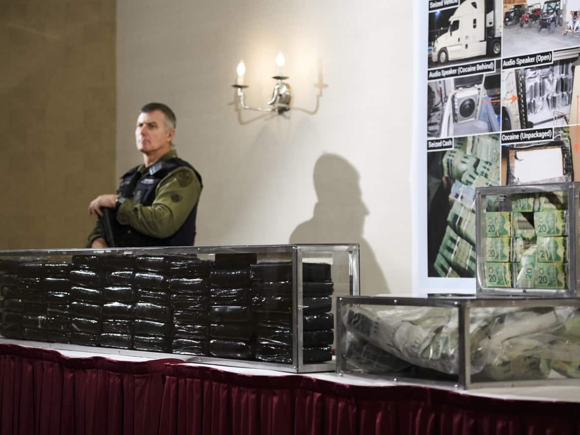 An Ontario Provincial Police officer guards 55 kilograms of cocaine and about $800,000 in Canadian currency seized by police during a press conference in Barrie, Ont., on Wednesday, April 3, 2019. (Nathan Denette/The Canadian Press - image credit)