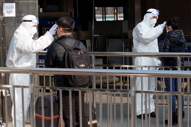 Workers take the body temperature of passengers before they enter the subway station outside the Beijing Railway Station in Beijing