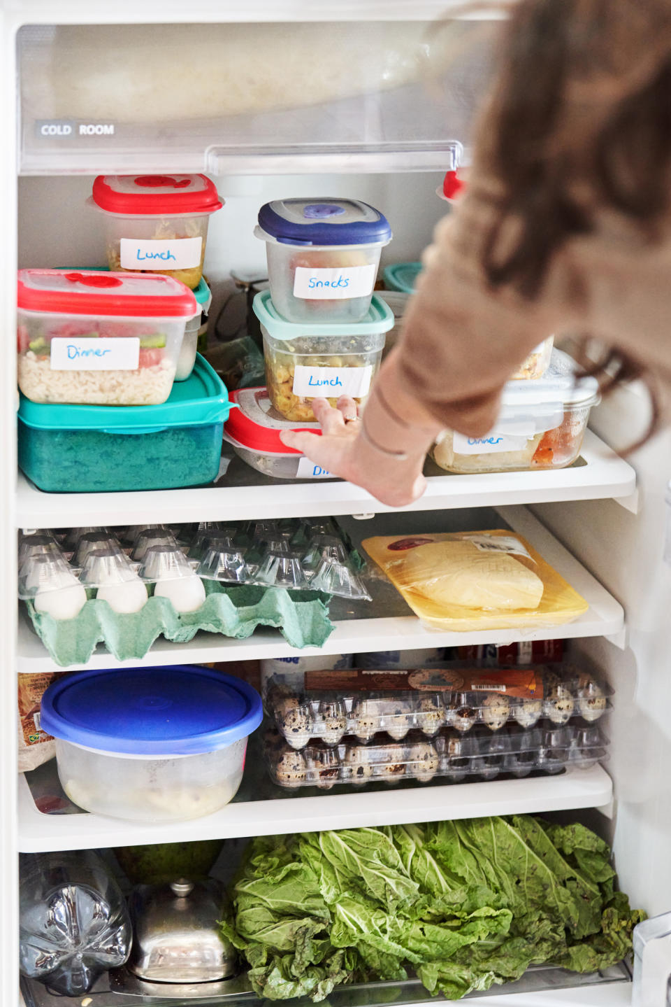 Person reaching into a fridge stocked with labeled containers and fresh produce