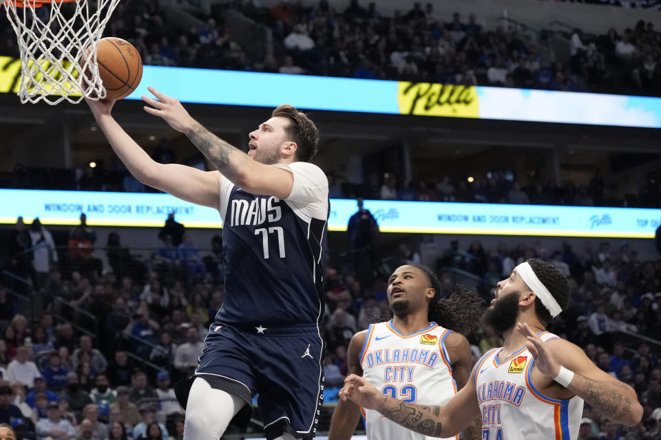 Dallas Mavericks guard Luka Doncic (77) leaps to the basket to take a shot after getting throgh Oklahoma City Thunder's Cason Wallace (22) and Kenrich Williams, right, in the first half of an NBA basketball game in Dallas, Saturday, Feb. 10, 2024. (AP Photo/Tony Gutierrez)
