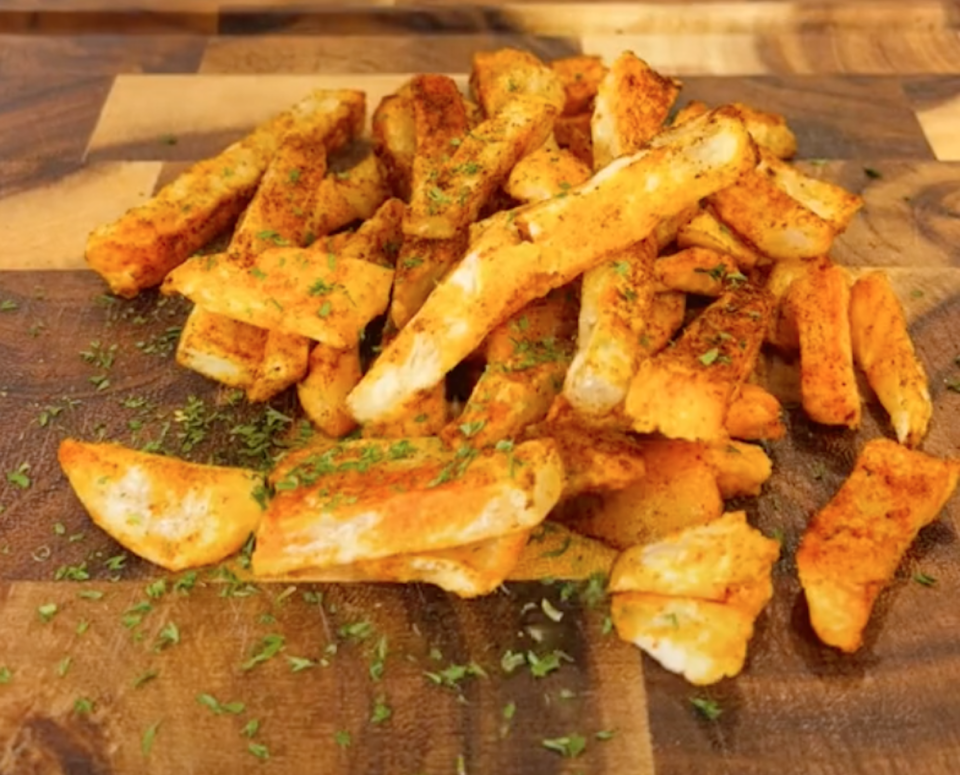 Perfect looking air fryer french fries scattered with herbs on a wooden bench.