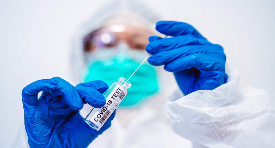 Doctor in protective gloves & workwear holding open test tube and taking out sampling swab for novel Covid-19 test in laboratory.