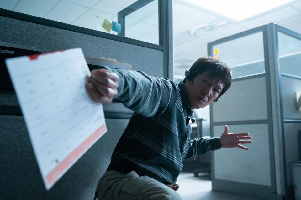 ke huy quan in everything everywhere all at once. he's crouched down near a cubicle wall, having caught a document behind him, and wearing earpieces