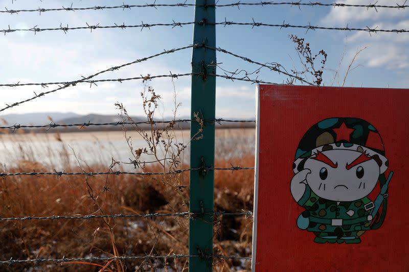 FILE PHOTO: A cartoon soldier is depicted on part of a warning sign on barbed wire on the Chinese side of the border between Russia, China and North Korea near the town of Hunchun