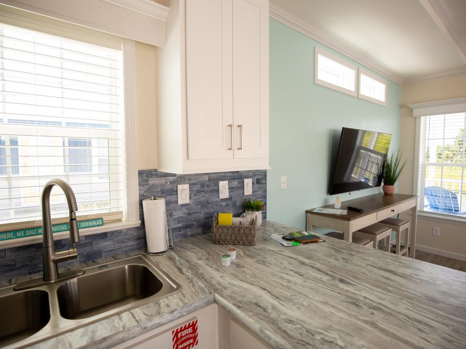 A kitchen with a sink, cabinets next to a TV and living room.