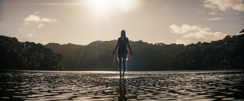 A woman levitates above a lake in silhouette