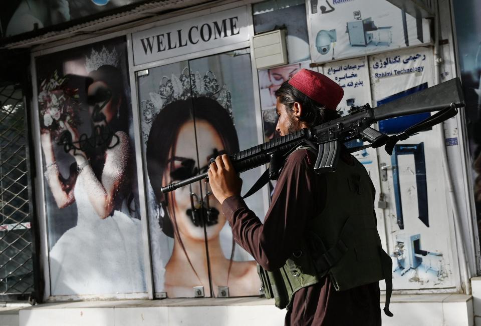 A Taliban fighter walks past a beauty saloon with images of women defaced using spray paint in Shar-e-Naw in Kabul, Afghanistan on August 18, 2021.