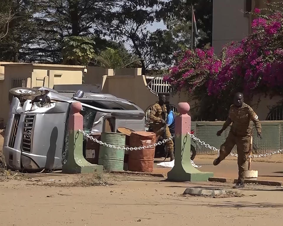 In this image made from video, Burkina Faso mutinous soldiers look at a wreaked car outside the Guillaume Ouedraogo military camp in Ouagadougou Monday Jan. 24, 2022. Mutinous soldiers said they detained Burkina Faso's President Roch Marc Christian Kabore on Monday, a day after rebellious troops seized a military barracks, setting off a series of gunbattles in the capital of the West African country. (AP Photo)