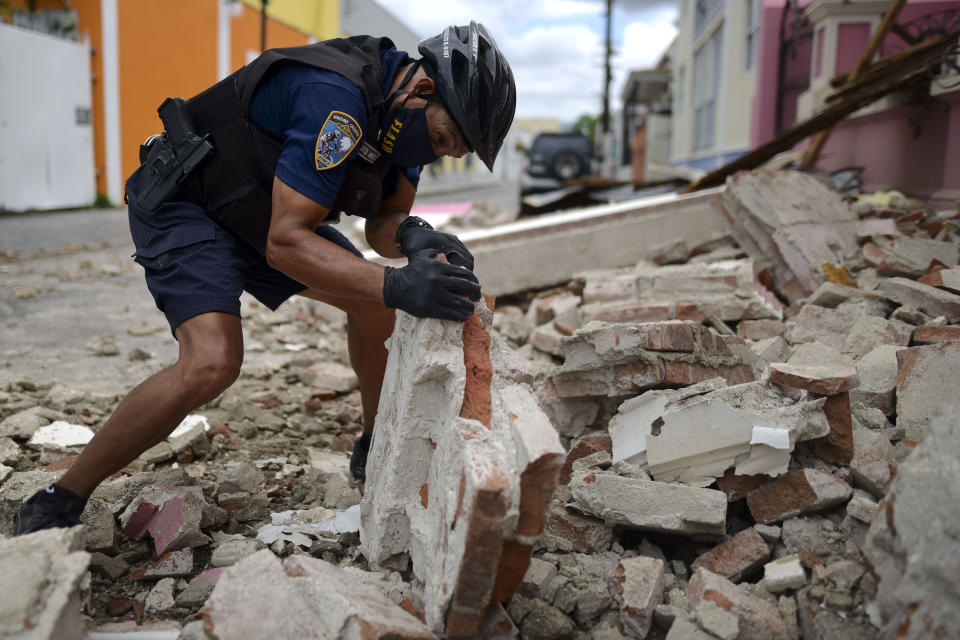 Un policía con una máscara protectora por el coronavirus, retira escombros dejados por un sismo de magnitud 5,4 en Ponce, Puerto Rico, el sábado, 2 de mayo del 2020. No hubo informes inmediatos de víctimas. (AP Foto/Carlos Giusti)