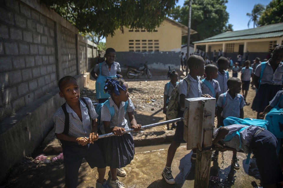 Students pump drinking water from a well, six months after a 7.2 magnitude earthquake in Les Cayes, Haiti, Wednesday, Feb. 16, 2022. Thousands of Haitians who lost their homes in the quake remain in camps, living in cramped shelters made of plastic and cloth sheets and corrugated metal. (AP Photo/ Odelyn Joseph)