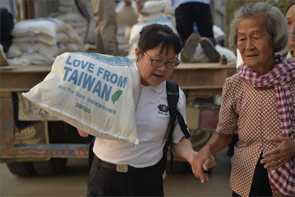 慈濟人醫會周真真護理師協助年長者搬大米，並牽著老奶奶的手。（圖為慈濟基金會提供）