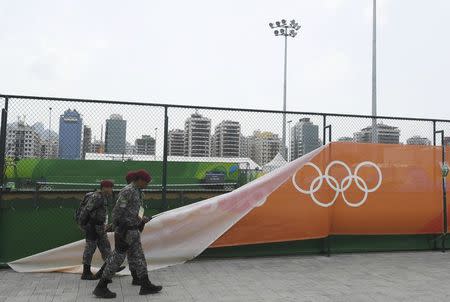 2016 Rio Olympics - Tennis - Olympic Tennis Centre - Rio de Janeiro, Brazil - 07/08/2016. Soldiers walk past a wind damaged banner outside the courts. REUTERS/Toby Melville