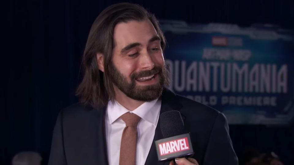 Jeff Loveness with long hair and a beard wearing a suit during an interview for the premiere of Ant-Man and The Wasp: Quantumania