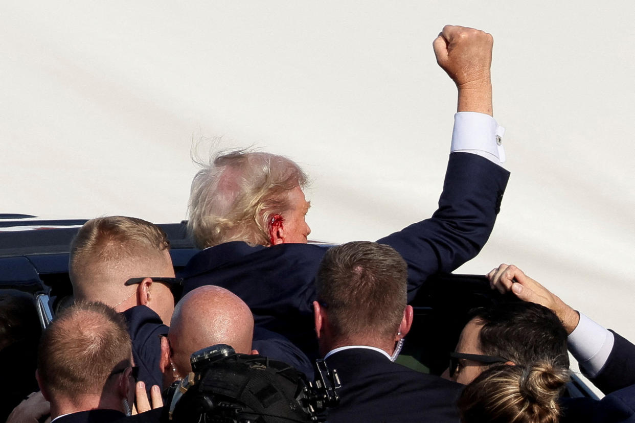 Trump, bleeding near the right ear, raises his fist as he is assisted to a waiting vehicle by the Secret Service after gunfire rang out. 