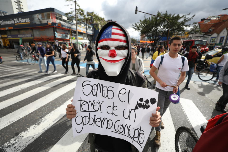 Un manifestante en contra del gobierno porta una máscara y sostiene un letrero durante una protesta en Bogotá, el miércoles 27 de noviembre de 2017. (AP Foto/Fernando Vergara)