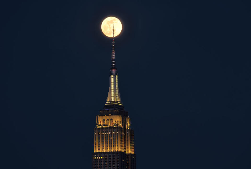 The tower at the top of a skyscraper overlaps the full moon