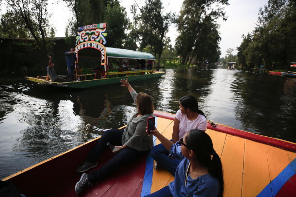 Colombian tourist Teresita Cortes Castillo, visiting with her two daughters, waves to Mexican revelers on another trajinera, the colorful boats typically rented by tourists, families, and groups of young people, in Xochimilco, Mexico City, Friday, Sept. 6, 2019. The usually festive Nativitas pier was subdued and largely empty Friday afternoon, with some boat operators and vendors estimating that business was down by 80% on the first weekend following the drowning death of a youth that was captured on cellphone video and seen widely in Mexico. Borough officials stood on the pier to inform visitors of new regulations that went into effect Friday limiting the consumption of alcohol, prohibiting the use of speakers and instructing visitors to remain seated. (AP Photo/Rebecca Blackwell)