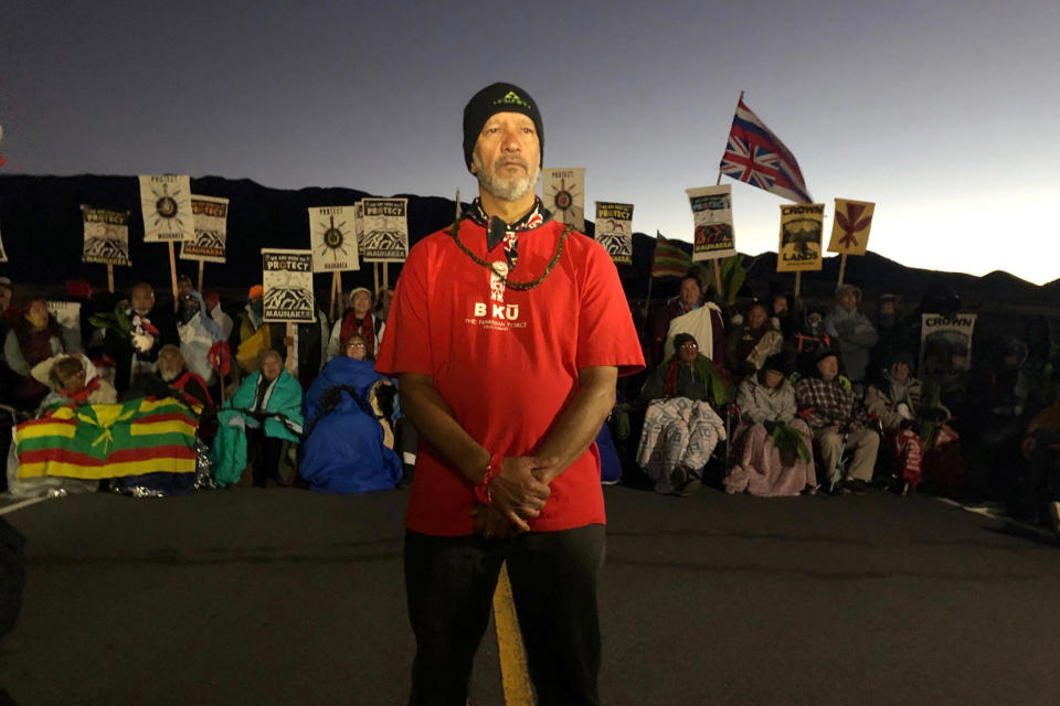 FILE - In this Monday, July 15, 2019, file photo, Dexter Kaiama, foreground, joins demonstrators gathered to block a road at the base of Mauna Kea, Hawaii's tallest mountain. For activists who say they're protecting Mauna Kea, the fight against the proposed Thirty Meter Telescope is a boiling point in Hawaiian history. (AP Photo/Caleb Jones, File)