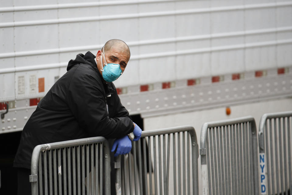 A medical worker wearing personal protective equipment due to COVID-19 concerns rests beside a refrigerated container truck functioning as a makeshift morgue, Tuesday, March 31, 2020, at Brooklyn Hospital Center in the Brooklyn borough of New York. The new coronavirus causes mild or moderate symptoms for most people, but for some, especially older adults and people with existing health problems, it can cause more severe illness or death. (AP Photo/John Minchillo)