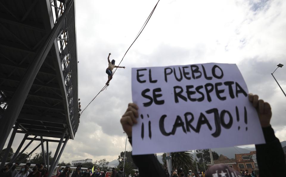 Un manifestante sostiene un cartel mientras estudiantes universitarios realizan acrobacias y otros bloquean la calle durante un paro nacional contra la reforma fiscal propuesta por el gobierno en Bogotá, Colombia, el miércoles 28 de abril de 2021. (AP Foto/Fernando Vergara)