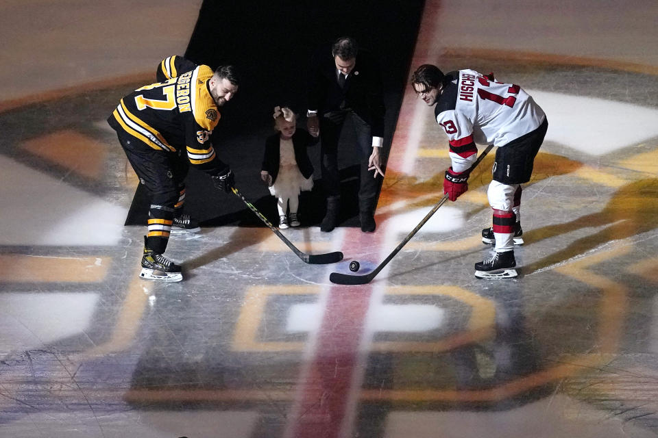 Former Boston Bruins goalie Tuukka Rask, center, holds his daughter Livia's hand as he drops the puck during a ceremony honoring his retirement, between Boston Bruins center Patrice Bergeron (37) and New Jersey Devils center Nico Hischier (13) at an NHL hockey game Thursday, March 31, 2022, in Boston. (AP Photo/Charles Krupa)