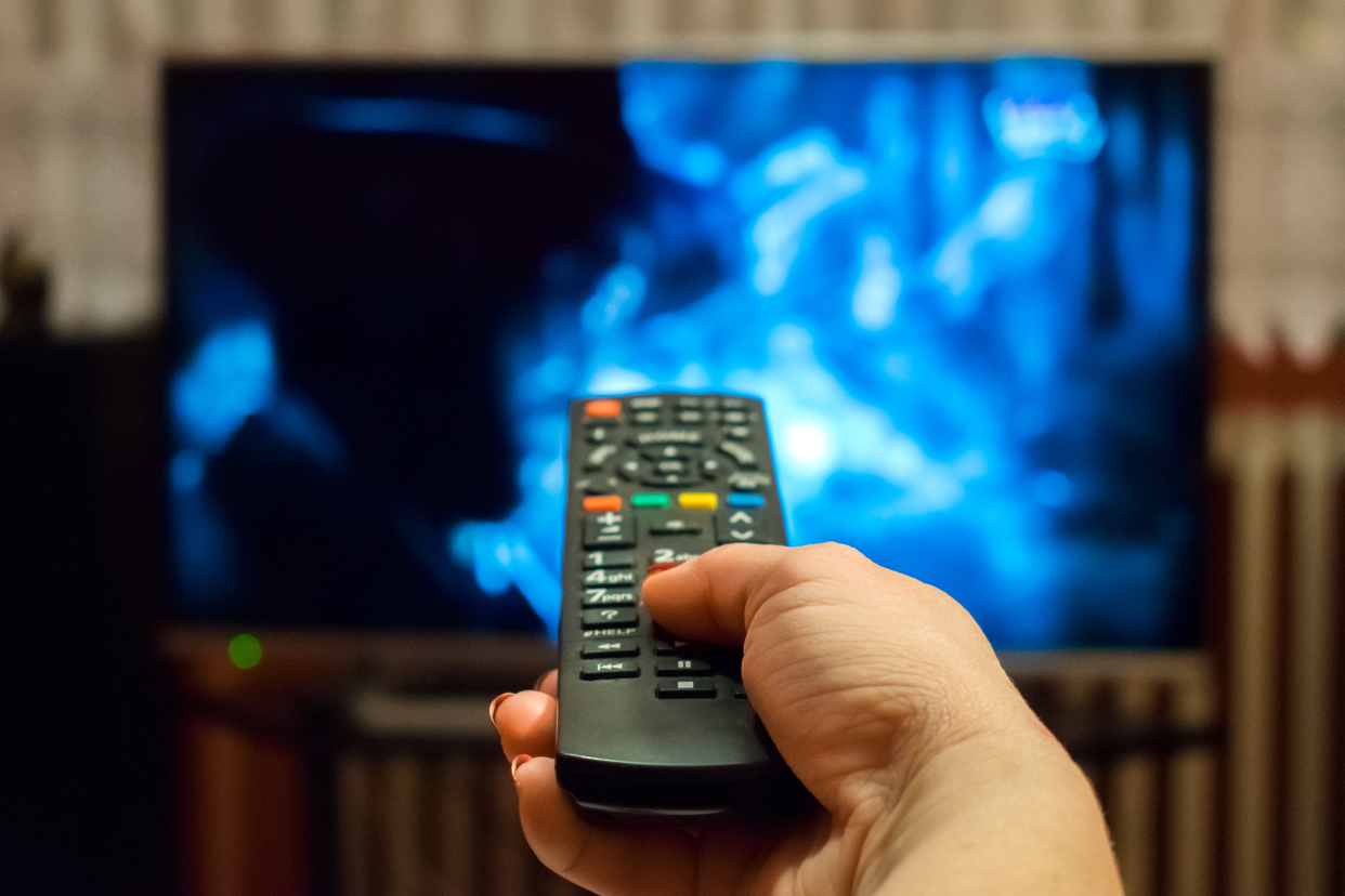 Closeup of hand holding a remote control and watching television