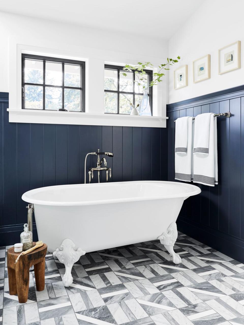 small bathroom with gray and white marble till floor, white clawfoot tub, navy wainscoting on bottom two thirds of wall