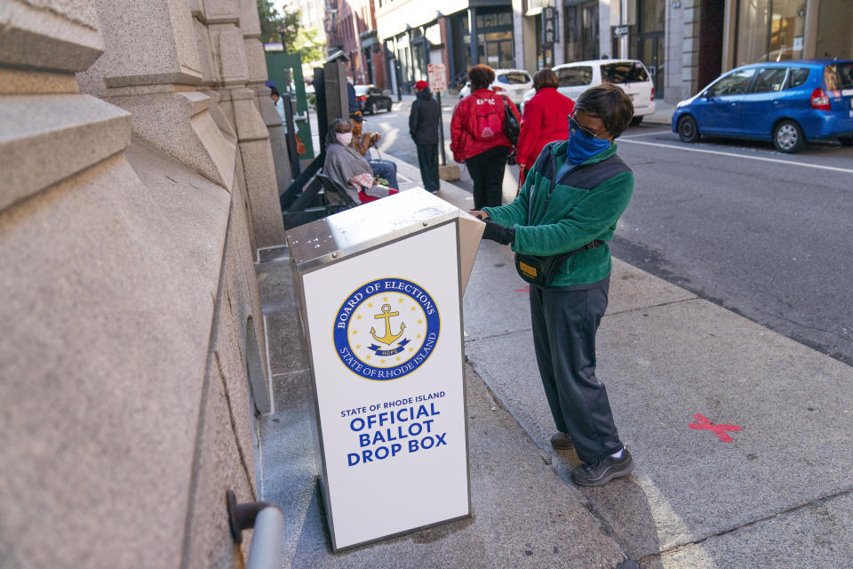 FILE - In this Oct. 14, 2020, file photo, Eva Abodoadji drops off a mail ballot into an official ballot drop box as voters wait in line at City Hall as in-person early voting begins for the general election in Rhode Island in Providence, R.I. As it has for more than 170 years, The Associated Press will count the vote and report the results of presidential, congressional and state elections quickly, accurately and without fear or favor on Nov. 3 and beyond. (AP Photo/David Goldman)