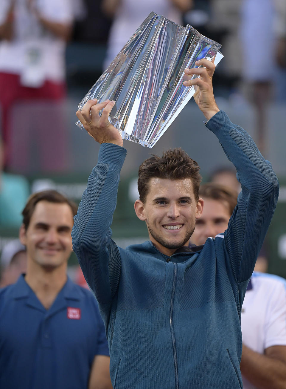 FILE - In this Sunday, March 17, 2019, file photo, Dominic Thiem, of Austria, foreground, raises a trophy over his head after defeating Roger Federer, of Switzerland, left, in the men's final at the BNP Paribas Open tennis tournament, in Indian Wells, Calif. Roger Federer has won one trophy so far in 2019, which puts him in a tie for the ATP lead, with 18 other players. That same sort of unprecedented parity is going on in the WTA, with 13 different champions from 13 tournaments. (AP Photo/Mark J. Terrill, File)