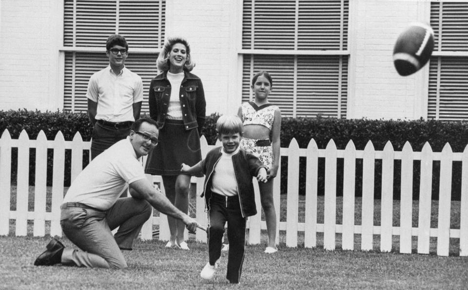 FILE - In this June 1, 1970, file photo, Kansas City Chiefs owner Lamar Hunt watches after holding the ball for his son, Clark, 5, to kick in the family backyard in Dallas. Behind them is Hunt's children by a former marriage, Lamar Jr. 13, left, and Sharon, 12, right. His wife Norma is at center rear. Lamar Hunt was a champion of Black rights during the Civil Rights era of the 1960s. He grew up in conservative circles yet formed his own opinions of right and wrong. And when his football-loving son was born in 1965, those principles that Hunt instilled in his football franchise became instilled in Clark, who years later would take succeed him as chairman of the Chiefs. (AP Photo/File)