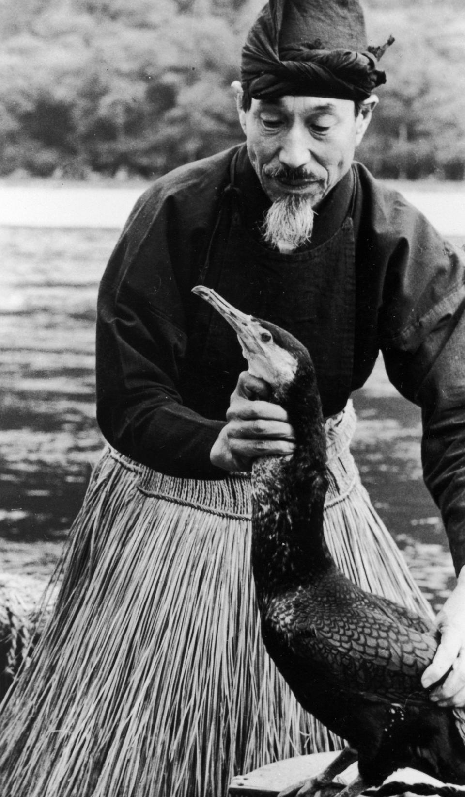 A black and white photo of a man holding a cormorant's neck.