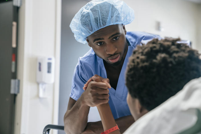 Doctor holding hand of boy in hospital bed. (Getty images)