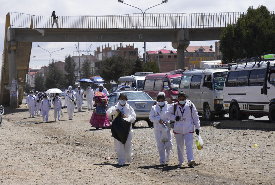 Los trabajadores de la salud caminan de regreso al centro de salud cercano para devolver su equipo de protección después de participar en una ceremonia de inicio de una campaña de vacunación contra el COVID-19 puerta a puerta en El Alto, Bolivia, el jueves 16 de septiembre de 2021. (AP Foto/Juan Karita)