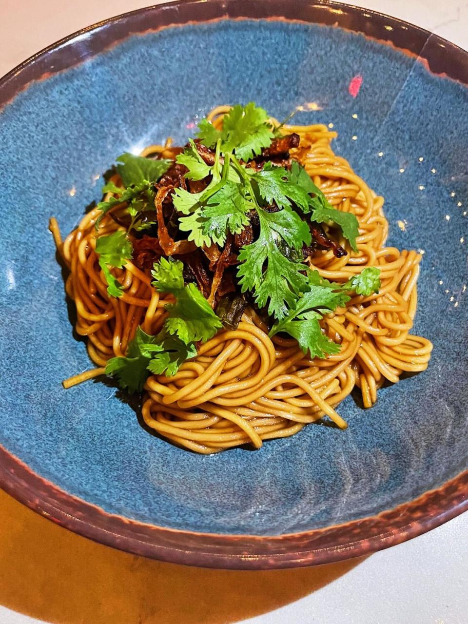 A blue ceramic bowl of sauced noodles under cilantro and crispy onions from the Airliner in Lincoln Heights.