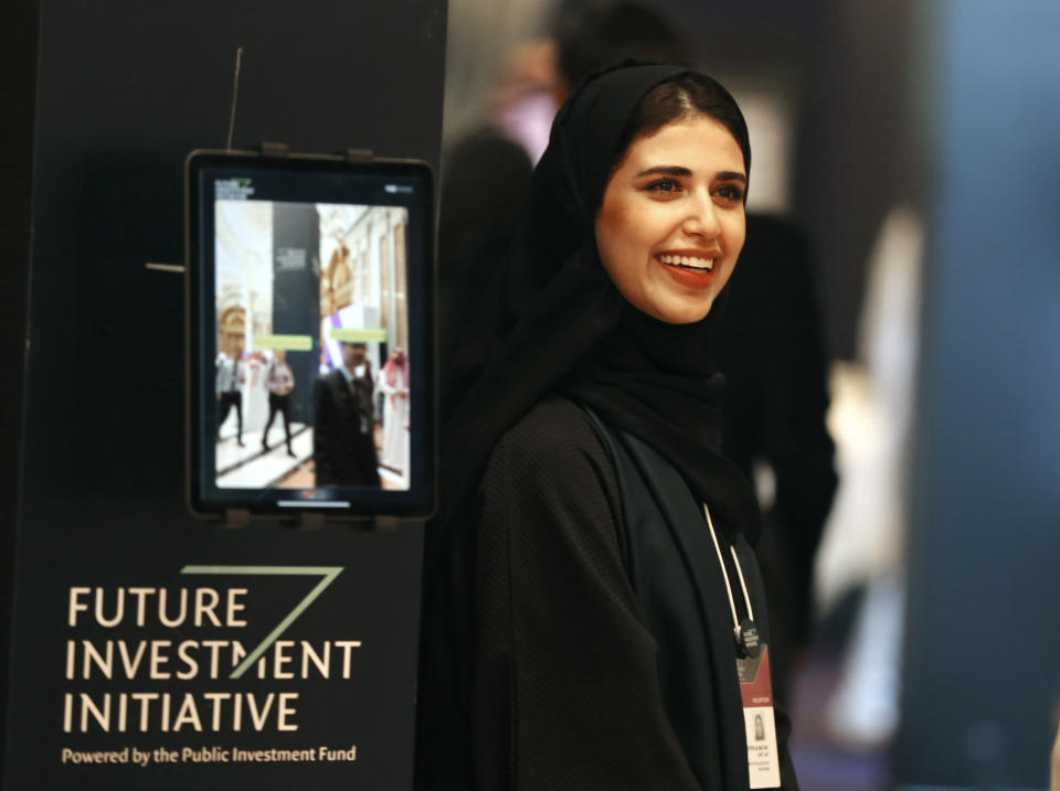 A Saudi organizer at the Future Investment Initiative conference, "FII", smiles as she welcomes participants, in Riyadh, Saudi Arabia, Tuesday, Oct. 29, 2019. The FII drew 6,000 people and international firms to Riyadh for a forum that's the brainchild of the 34-year-old Prince Mohammed. (AP Photo/Amr Nabil)